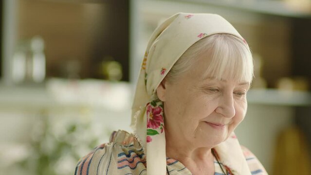 Portrait of Ukrainian senior woman wearing headscarf and waiting for son at home