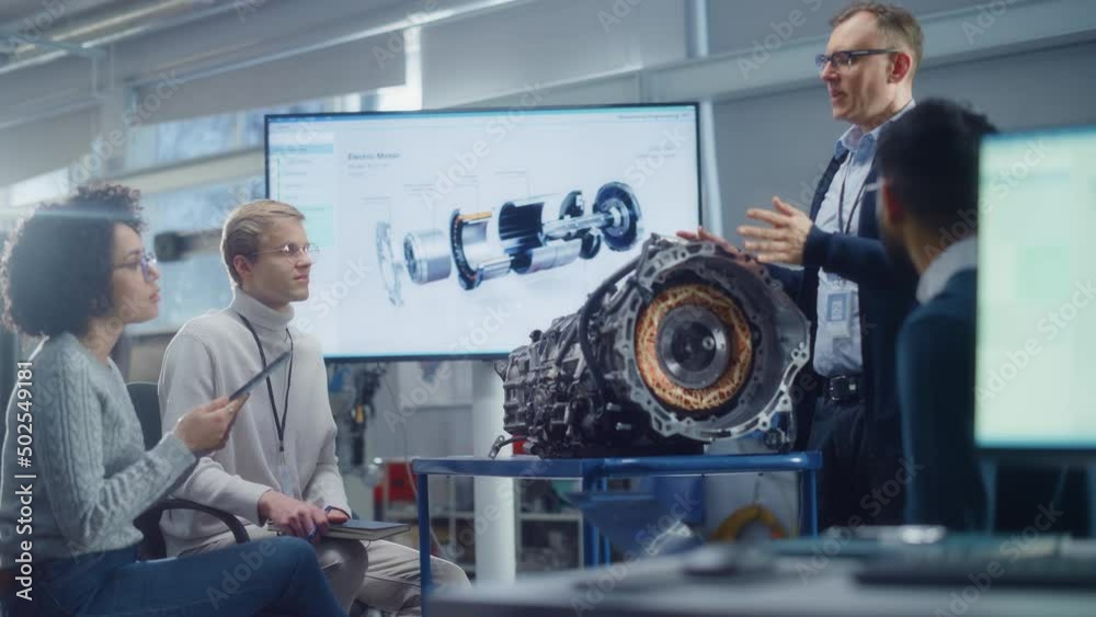 Poster chief engineer talks to team of young diverse specialists while analysing engine at the research lab