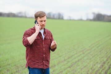 Young handsome farmer walking on farmland, and talking on cell phone