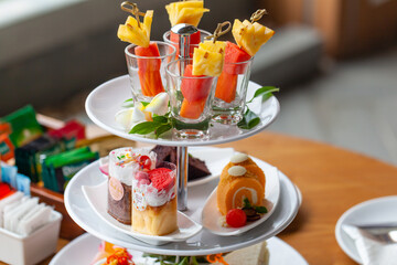 Colorful tropical mixed fruit skewers on white plate. Fresh summer fruits on bamboo sticks. Pineapple, watermelon and papaya on wooden kebabs, snacks, cakes, cookies afternoon tea set two persons.