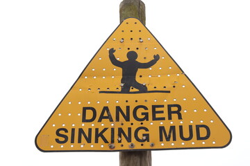'DANGER SINKING MUD' sign against overcast sky background