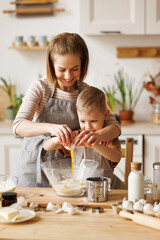 Happy woman and son cooking together in kitchen - obrazy, fototapety, plakaty