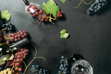 Top view close up of bottle, two wine glasses, fresh grapes and leaves on black studio background...
