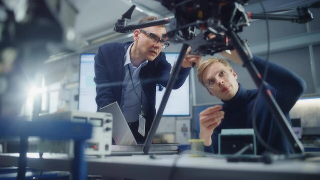 Chief Engineer Look at Drone Attentively While Discussing Design with Promising Scientist. Manufacturing Facility that Creates Great Products. Slow Motion