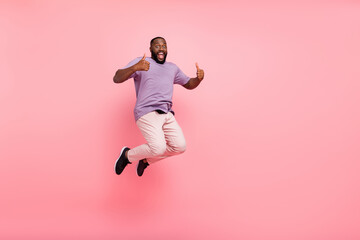 Fototapeta na wymiar Photo of excited pretty guy wear purple t-shirt jumping high thumbs up empty space isolated pink color background