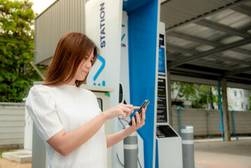 Fototapeta na wymiar A woman is using a phone to operate an electric car charger.