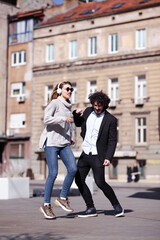 Young business colleagues dancing together with headphones after work. Happy friends jumping and fooling around outdoors