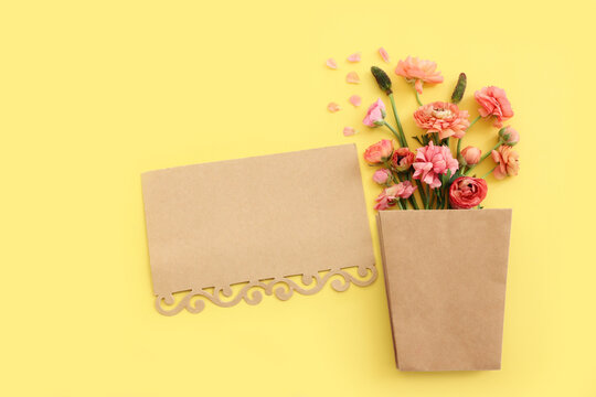 Top view image of pink flowers composition and empty note over yellow pastel background