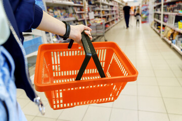 A shopping basket in a woman hand in a grocery hypermarket. Selective focus. Copy Space