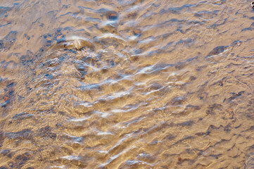 The bottom of the river with fine sand. Current, waves and wind. Water background. Sun glare.