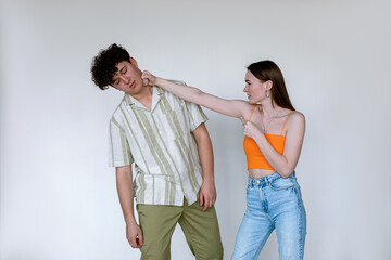 Portrait of young couple posing on white background. Young displeased woman punching fainting man with closed eyes.