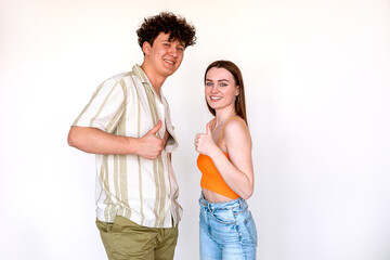 Portrait of young joyful couple posing on white background. Young curly smiling man and woman showing thumbs up sign.