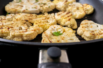 Cauliflower steak with spices cooked in pan. Vegetable meat substitute.