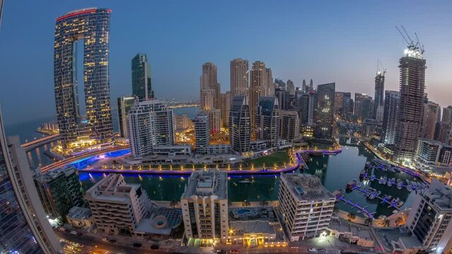 Panorama of Dubai Marina with several boats and yachts parked in harbor and skyscrapers around canal aerial night to day timelapse.
