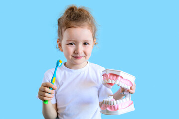 Little cute funny girl holding tooth jaw, toothbrush. Kid training oral hygiene. Child learning...