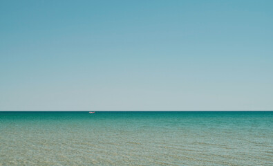 Fototapeta premium Sea panorama in shallow water with sun reflection in water, vast open sea with clear sky, ripple wave and calm sea with beautiful sunlight. Red boat is visible in distance. Wallpaper or banner idea