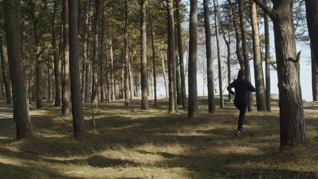 Young woman jogging off road among trees in forrest on a warm summer day in slow motion. Running away from the camera into the horizon. Static wide angle shot in slow motion and 4K.