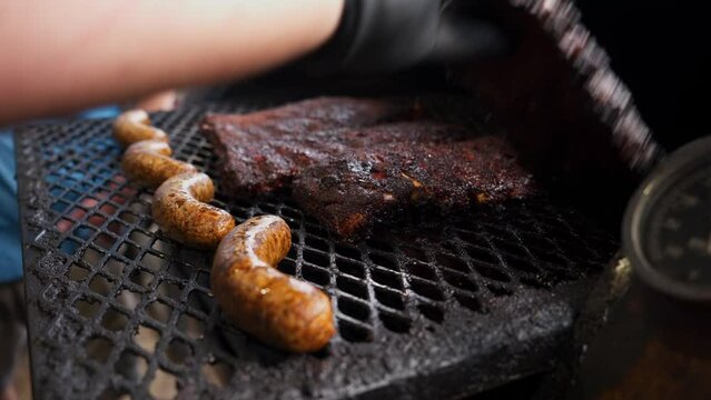 Barbecue pitmaster adjusts and flips racks of ribs on barbeque pit grates, slow motion 4K