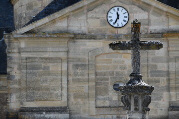 Old stone cross facing a massive construction with a clock in front.