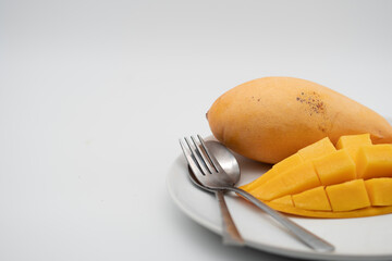 The mango slice is cut into cubes on a white plate. There are spoons and forks placed ready to eat. In the white background. Side view. workspace.