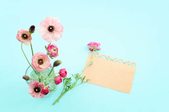 Top view image of pink flowers composition and empty note over blue pastel background