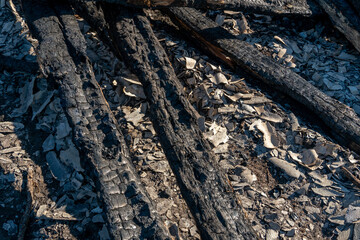 A wooden house in the village burned down because of a forest fire. Charred boards and various things lie on the ground, covered with ash and smoke.