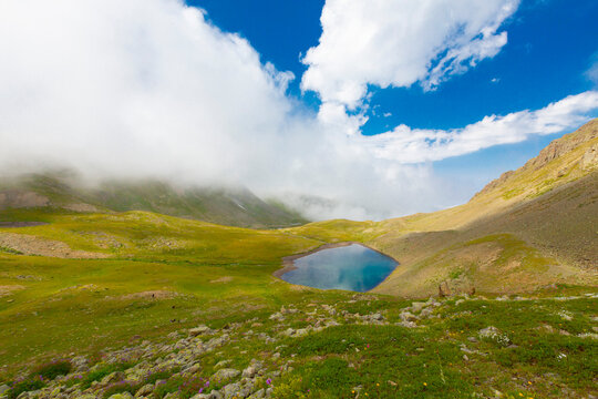A lake in mountains, natural landscape, green meadows, snowy mountains, blue sky, winter season. Hakkari Cilo Sat Lakes