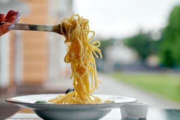 delicious pasta on a fork in a summer cafe with a picturesque background