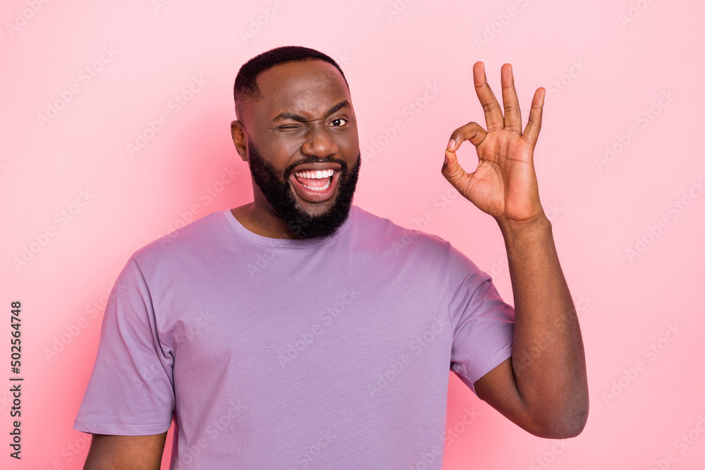 Wall mural photo of sweet excited guy dressed violet t-shirt showing okey winking isolated pink color backgroun