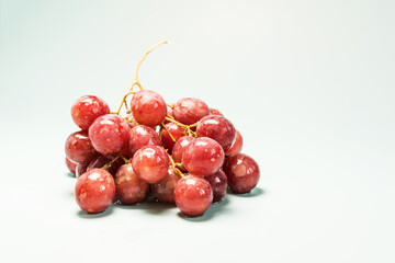 A branch of red grapes with water drops on a light blue background close-up in natural light.