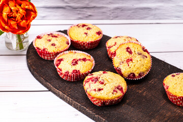 several currants muffins served on an old wooden board with bouquet of flowers