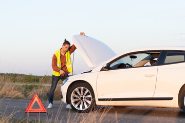 Man looking a broken car on the side of the road in an empty landscape with open car hood trying to fix it