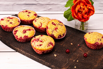 several currants muffins served on an old wooden board with bouquet of flowers