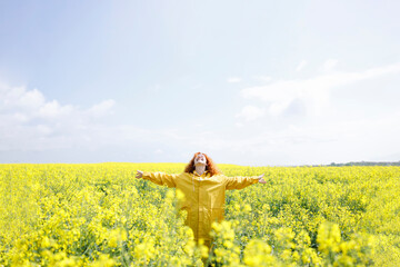 Grateful woman, being happy for a sunny summer day in a field of beautiful rapeseed flowers