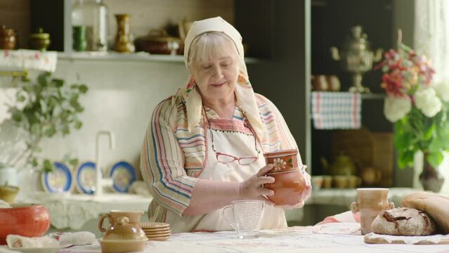 Grandmother pouring milk into the glass from crock in the country