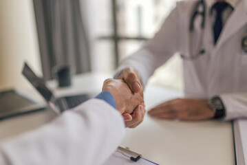 Female doctor shaking hands with patient while sitting at desk in clinic. Focus on the hands - handshake.