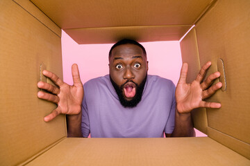 Low angel bottom view photo of funky shocked guy dressed violet t-shirt looking inside paper box isolated pink color background