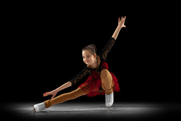 Beautiful girl, little female figure skater in beautiful stage attire skating isolated on black background in spotlight. Concept of movement, sport, beauty. © master1305