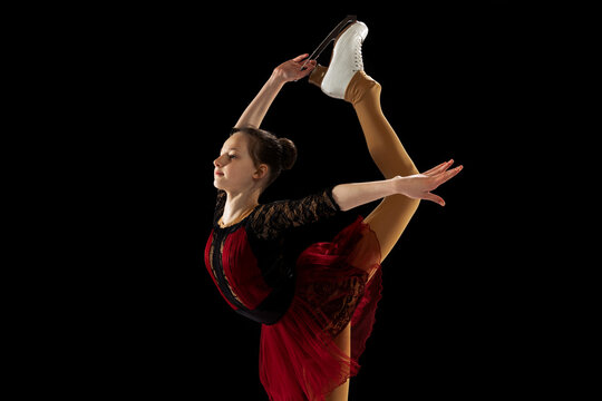 Studio shot of little female figure skater in beautiful stage attire skating isolated on black background in spotlight. Concept of movement, sport, beauty.