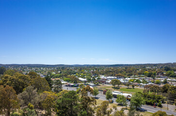 Fototapeta na wymiar Aerial view of trees, roads, and suburban houses in Ballarat against the cloudless blue sky. Background texture of landscape of an Australian regional town. VIC Australia