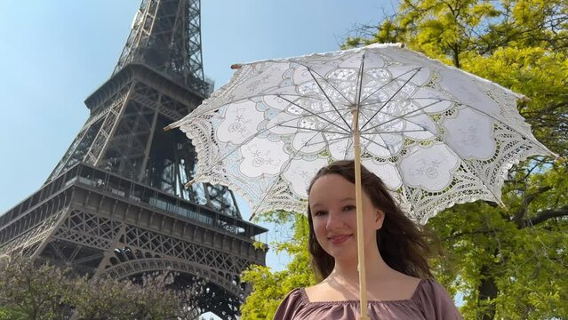 a cheerful teen girl stands against the backdrop of the Eiffel Tower she raised her hand, you can advertise a travel agency trip to Paris France. girls in the hands of an openwork umbrella