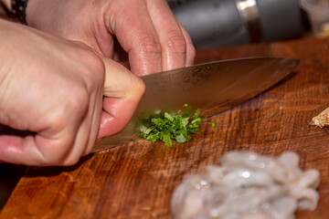 the cook cuts parsley and dill on a wooden board. cooking in a restaurant, chef's hand cutting greens on a wooden board, vegan salad with parsley
