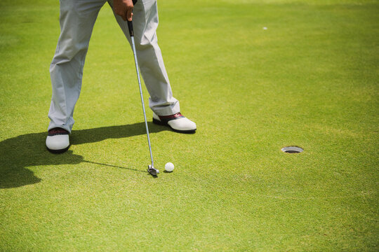 The golfer places the golf ball on the golf green into the hole.