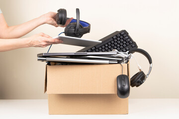 Woman hands put laptop computer and headphones in box full old used computers and gadget devices...