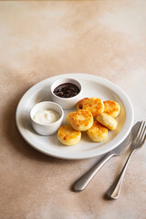 Cottage cheese pancakes, syrniki, ricotta fritters on white ceramic plate with sour cream and jam. Healthy and delicious morning breakfast. Beige background. Food for kids. Ukrainian food.