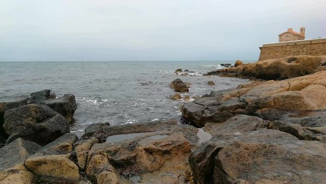  Church of the Island of Tabarca and waves of the sea on the coast with rocks