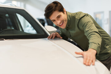 Positive millennial Caucasian guy touching new white car, selecting automobile at dealership store, copy space