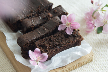 Homemade chocolate brownies decorated with pink flowers on white paper with light background. Brown...
