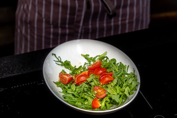 The chef prepares a salad of arugula and cherry tomatoes in the restaurant kitchen