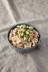 Homemade Olivier salad in a Bowl on a white wooden background, side view.